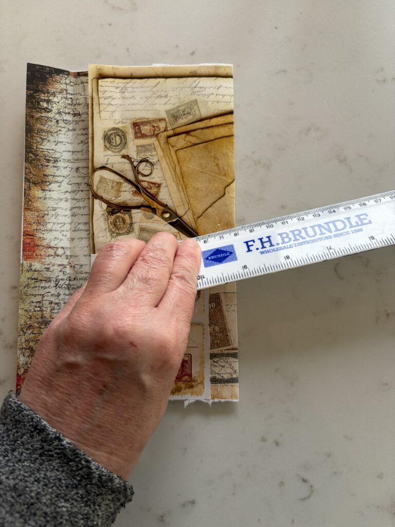 Scoring the outside of an old envelope covered in junk journal ephemera using a ruler