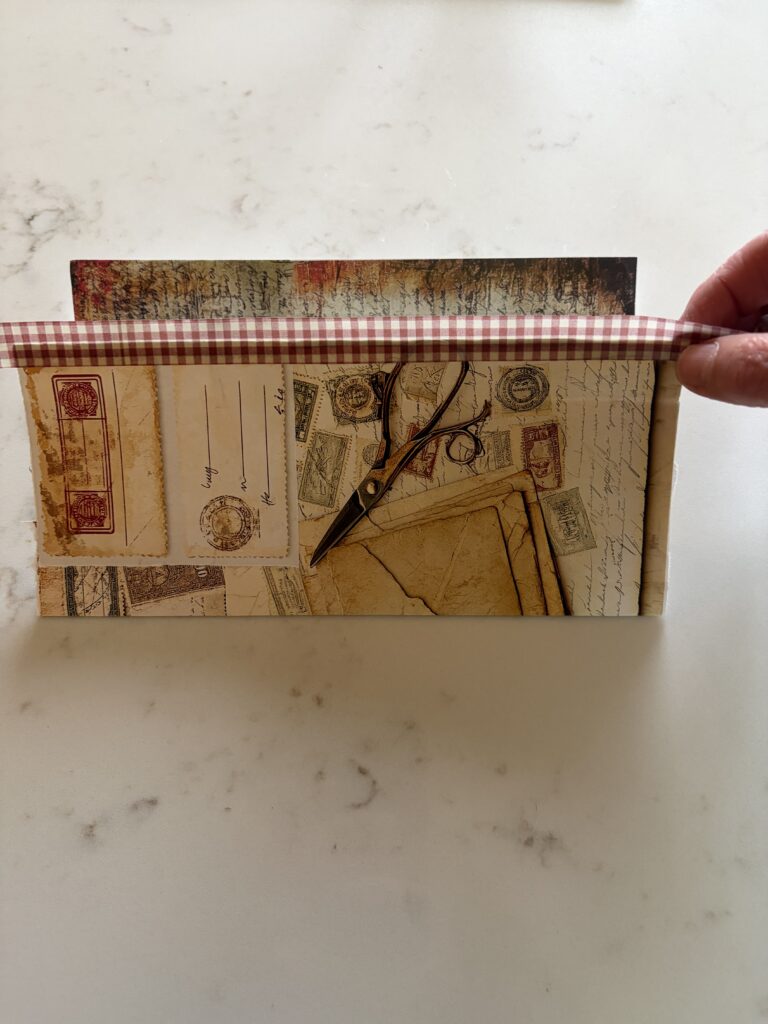 Adding washi tape to the edge of an old envelope covered with junk journal ephemera