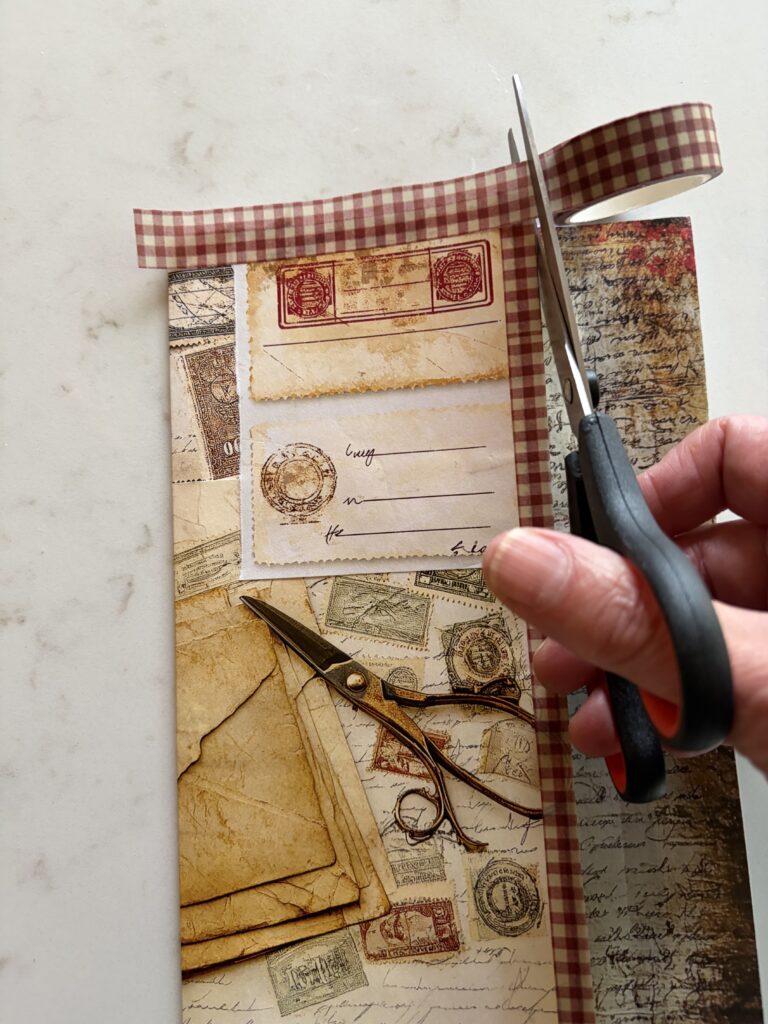 Adding washi tape to the side of an old envelope covered with junk journal ephemera